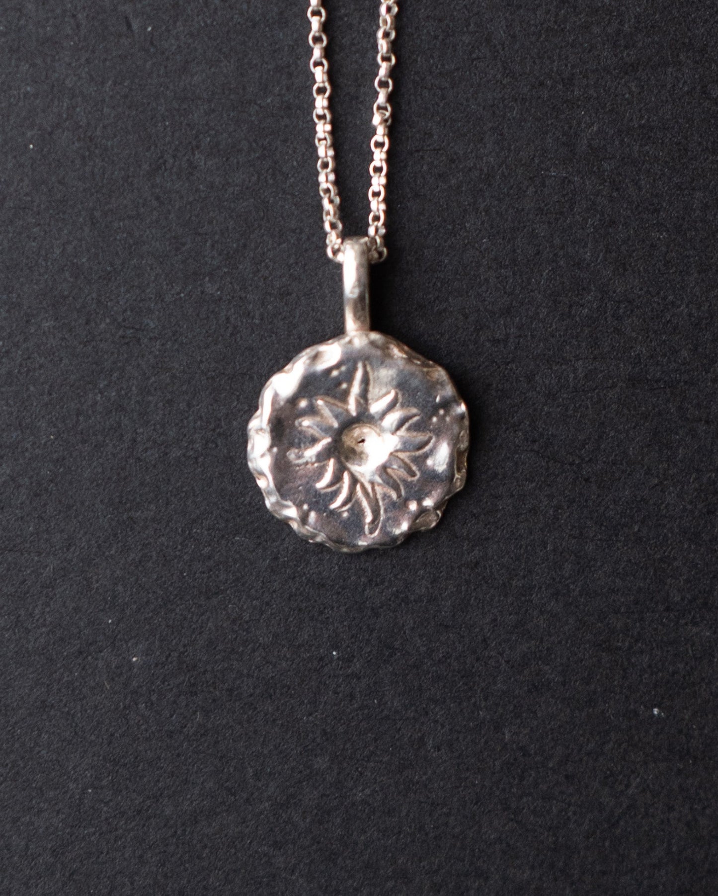 Silver sun pendant necklace on a black background
