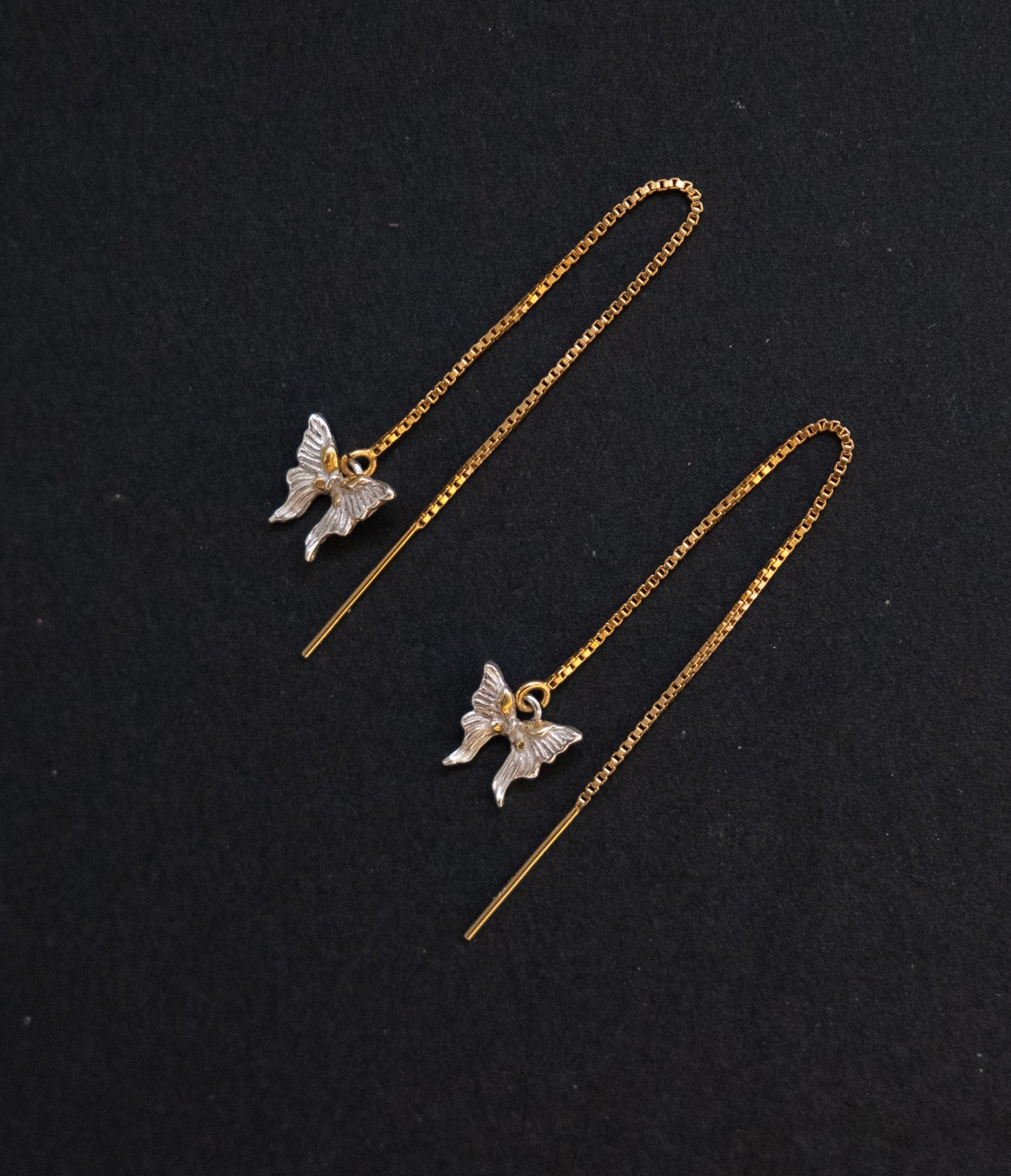 Butterfly-shaped earrings on thin gold chains against a black background