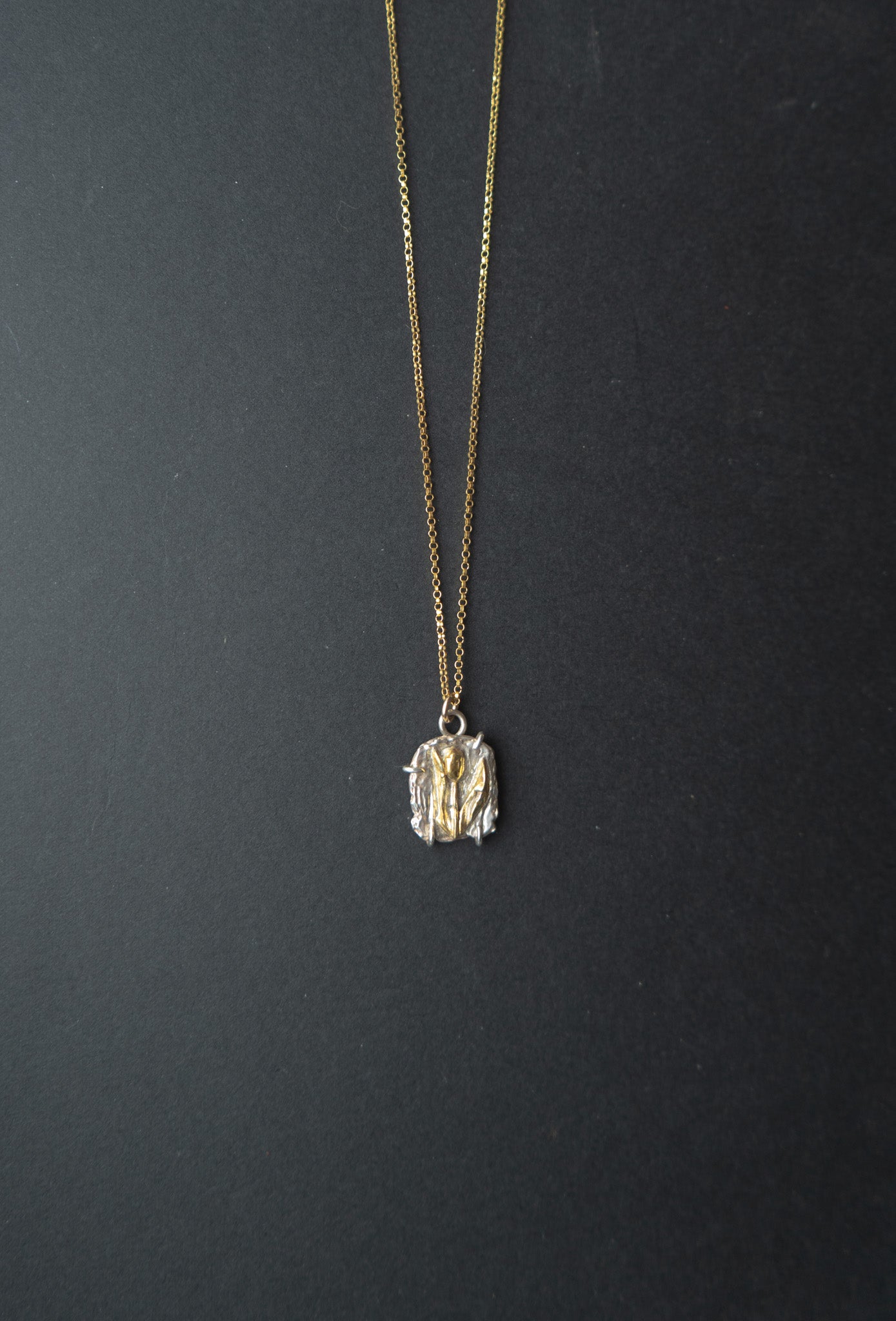 Gold and silver necklace with a pendant on a black background

