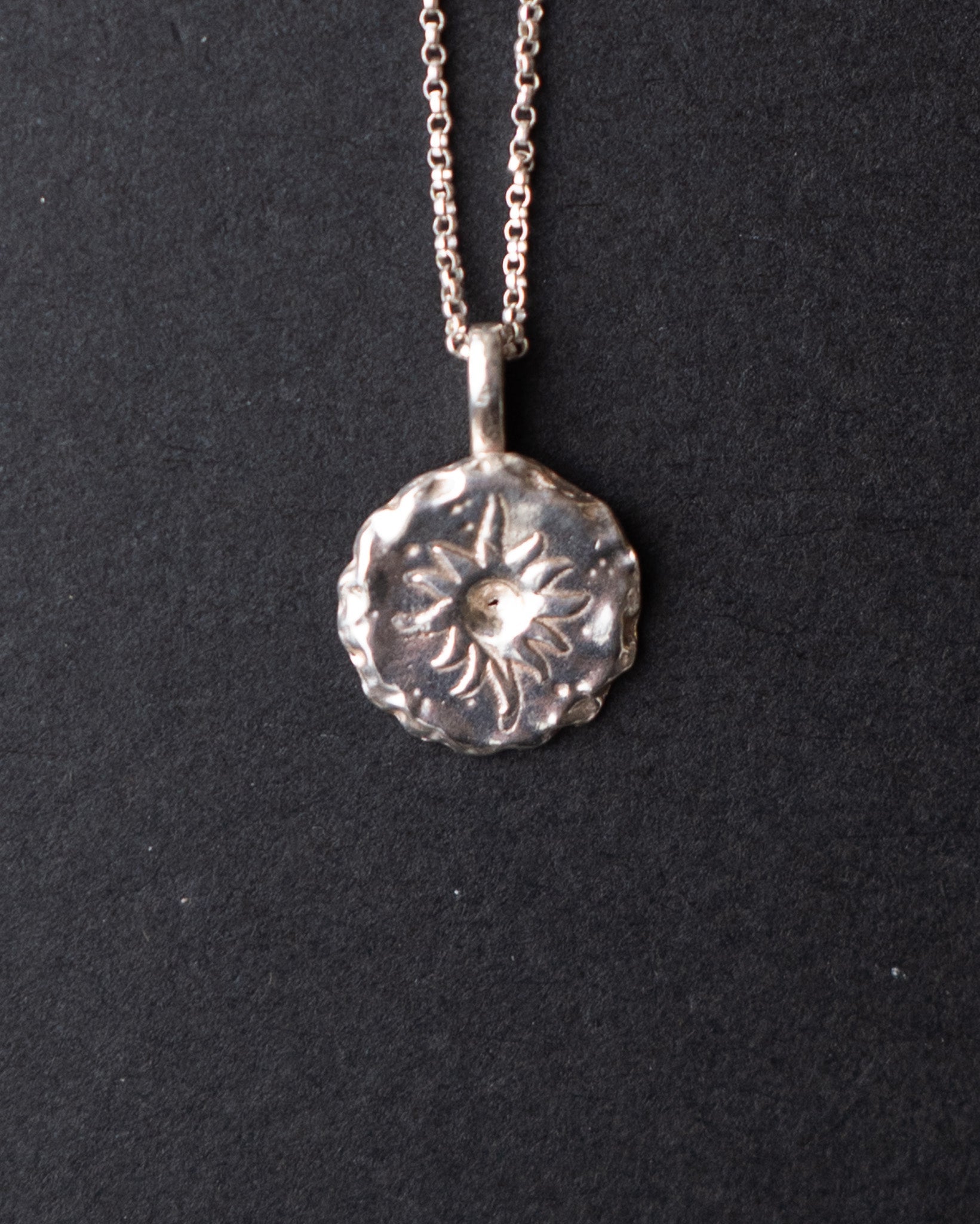 Silver sun pendant necklace on a black background