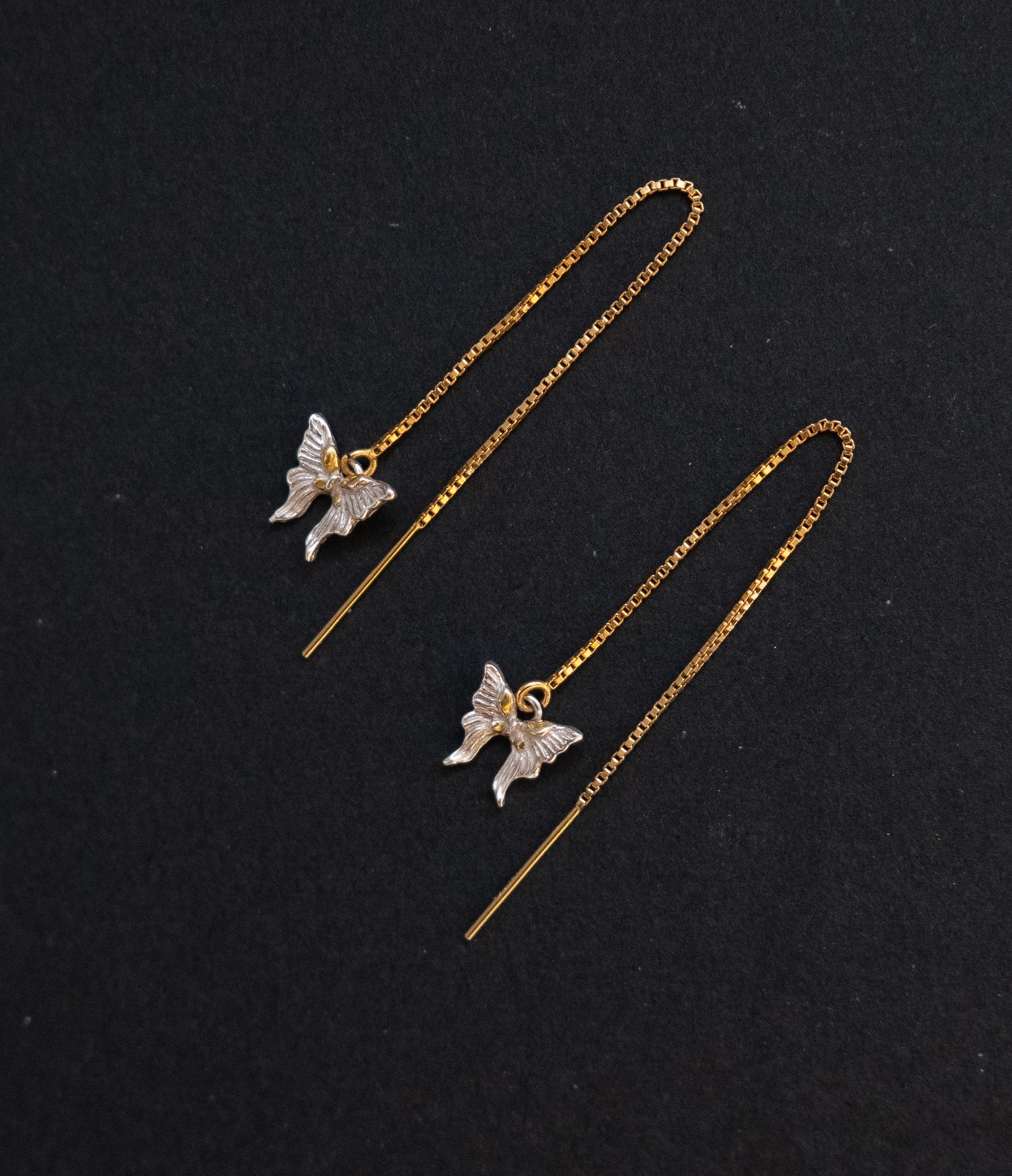 Butterfly-shaped earrings on thin gold chains against a black background