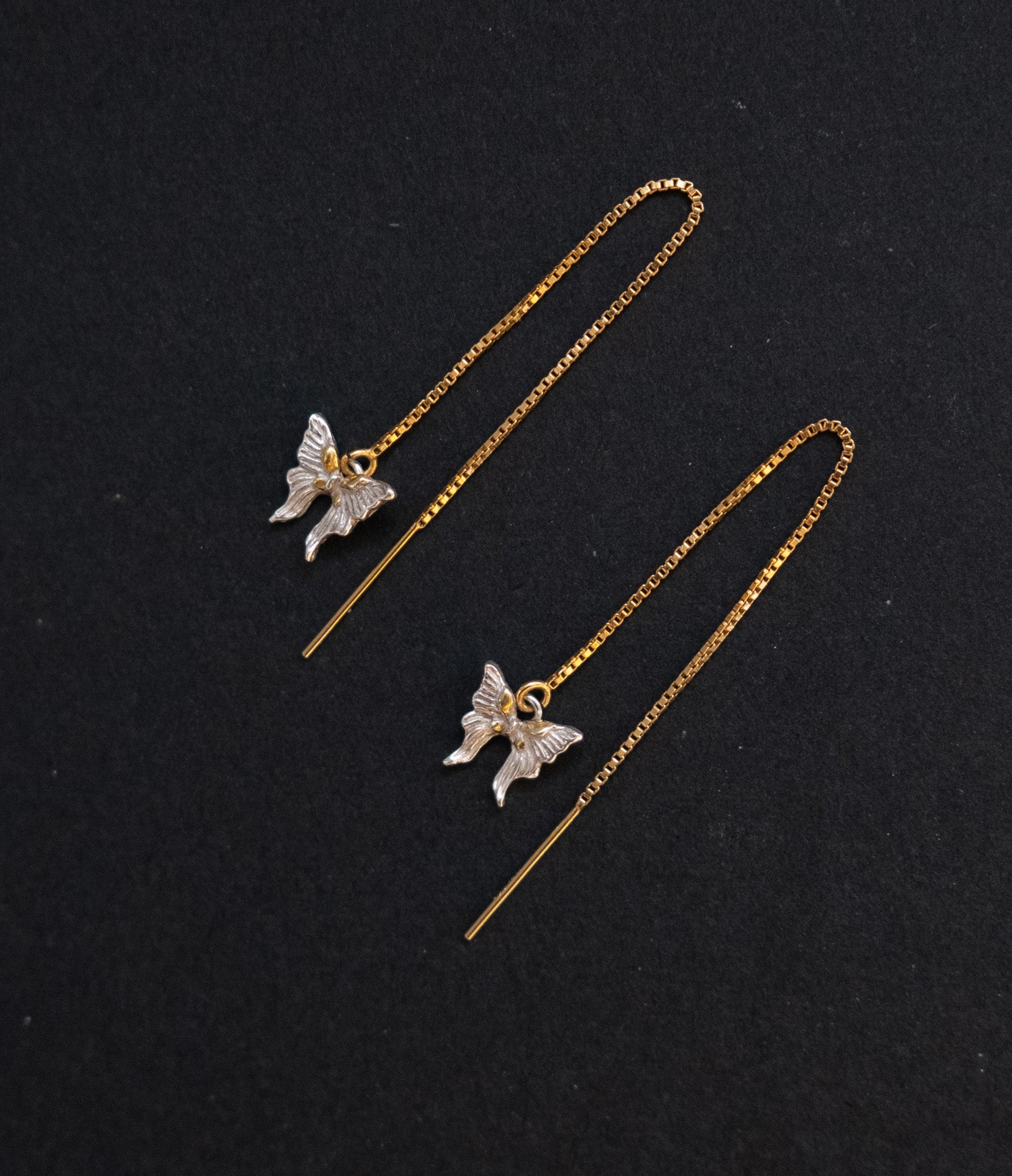 Butterfly-shaped earrings on thin gold chains against a black background